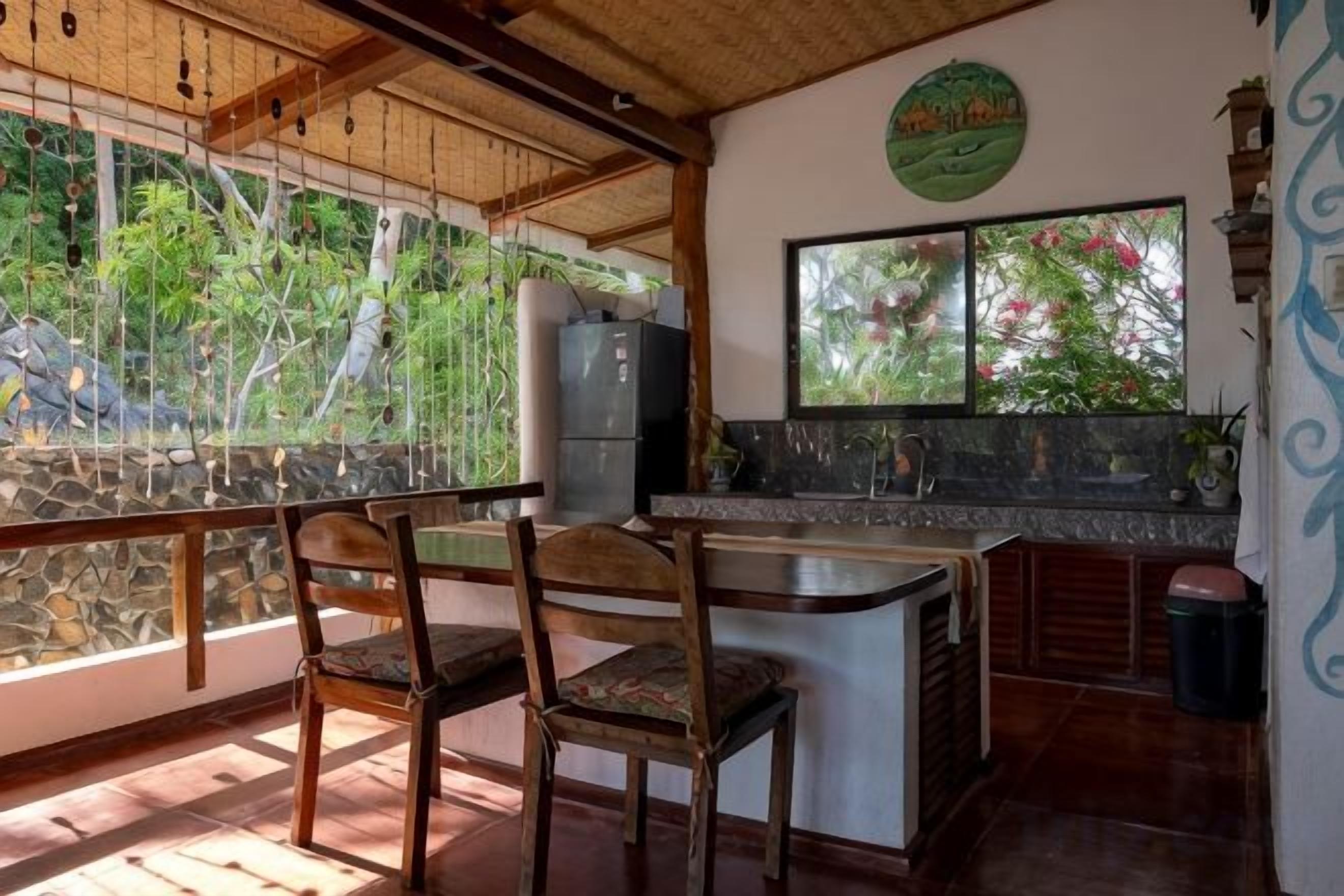 Een keuken met een stenen aanrecht, houten stoelen en uitzicht op groen door een raam.