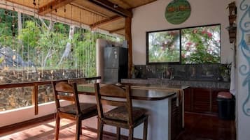 Een keuken met een stenen aanrecht, houten stoelen en uitzicht op groen door een raam.