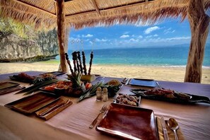 Een eettafel gedekt met verschillende gerechten en spiesjes, met uitzicht op een strand.