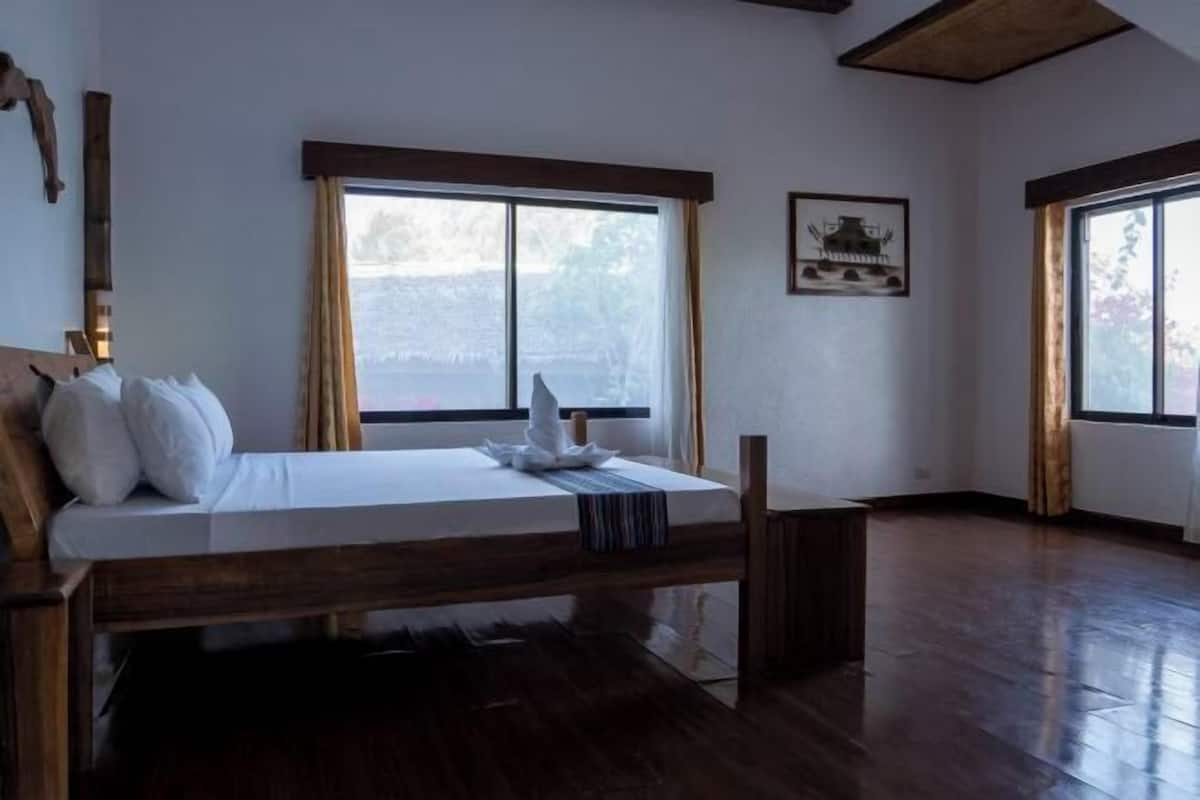 Une chambre avec un lit en bois, de grandes fenêtres et un tableau encadré au mur.