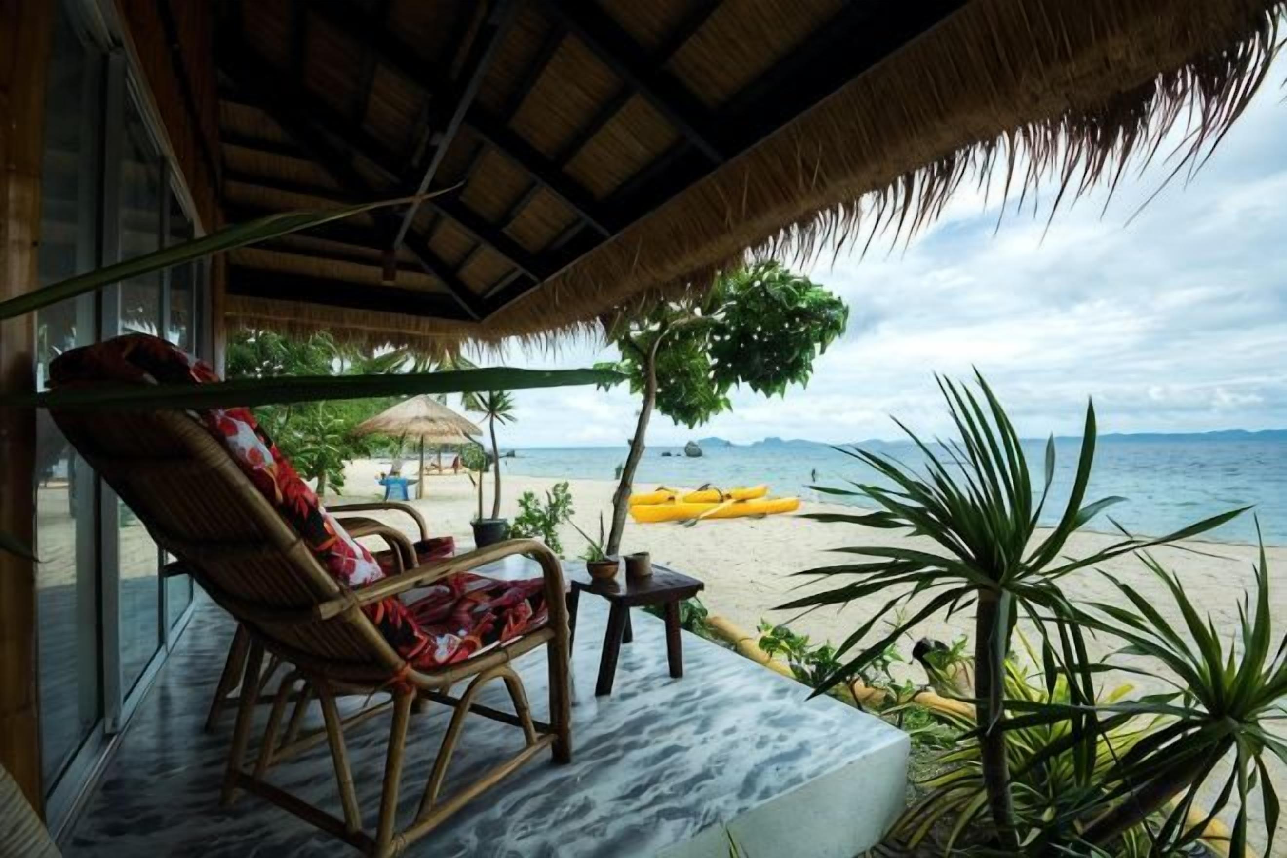 Un salon de plage doté d’un toit de chaume, d’un fauteuil en osier et offrant une vue sur la mer.