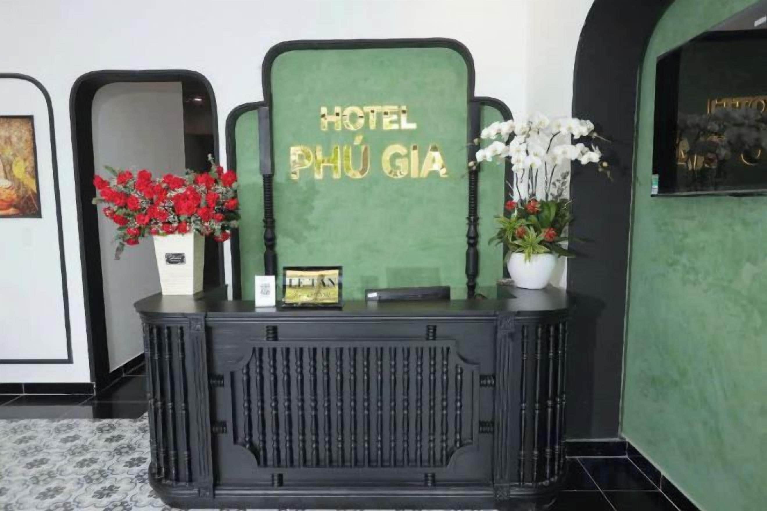 Una recepción con un letrero que dice 'HOTEL PHÚ GIÁ' y dos floreros, uno con flores rojas y otro con flores blancas.