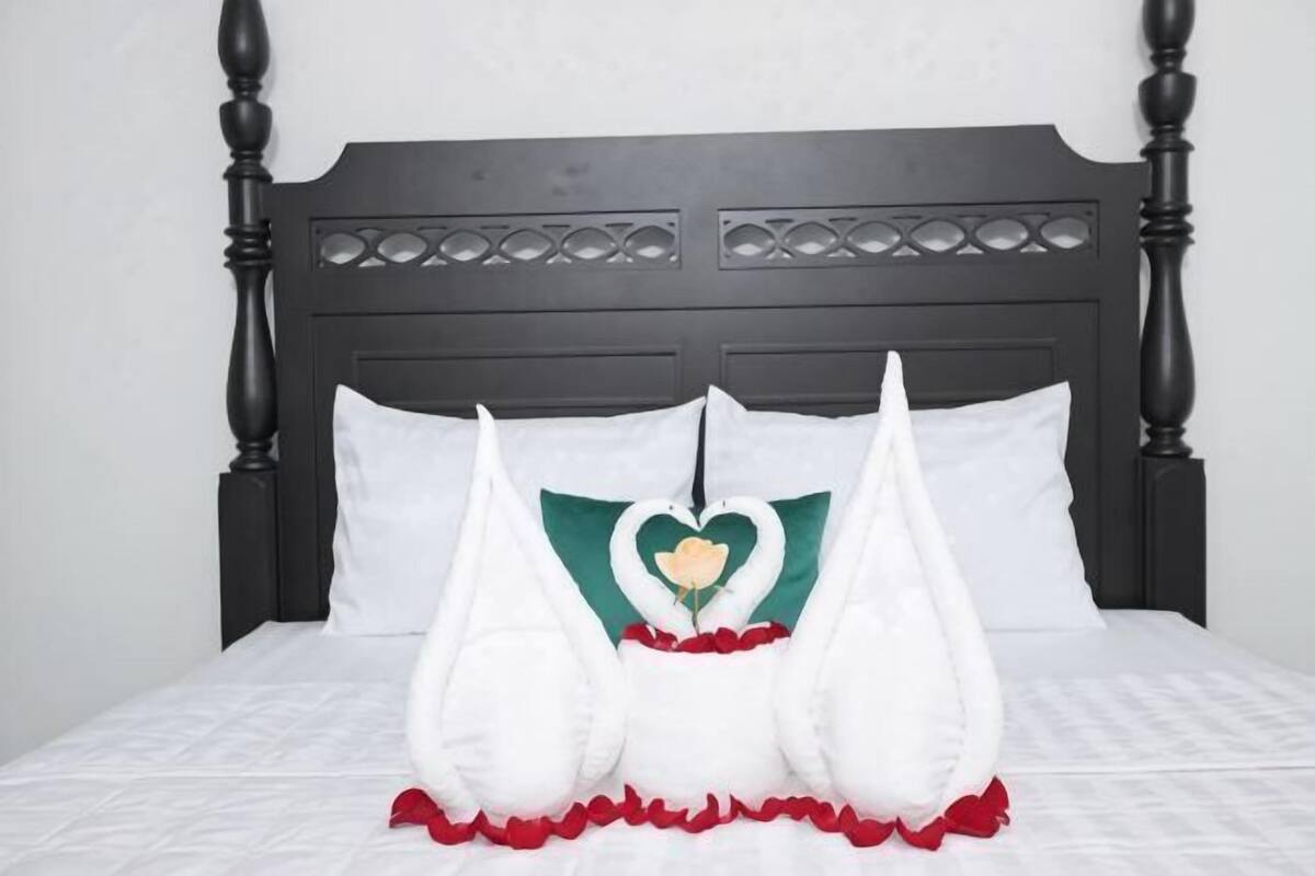 A bed with a dark wooden headboard, white bedding, and decorative pillows with a heart design.