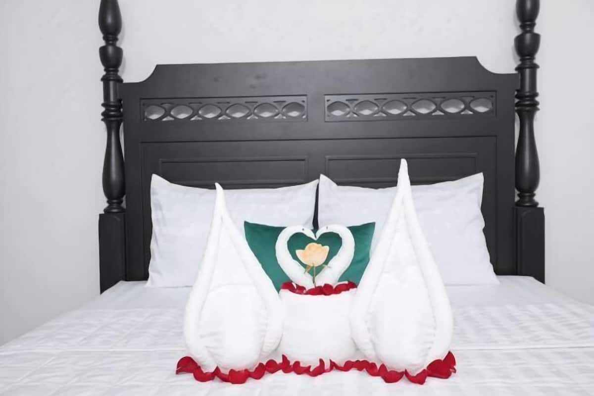 A bed with a dark wooden headboard, white bedding, and decorative pillows with a heart design.