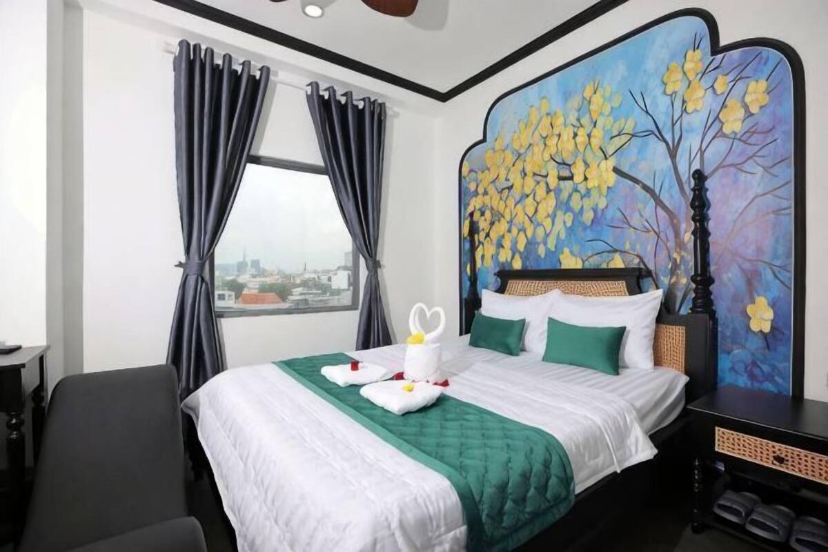 A hotel room with a bed, a view through the window, and a painting on the wall.