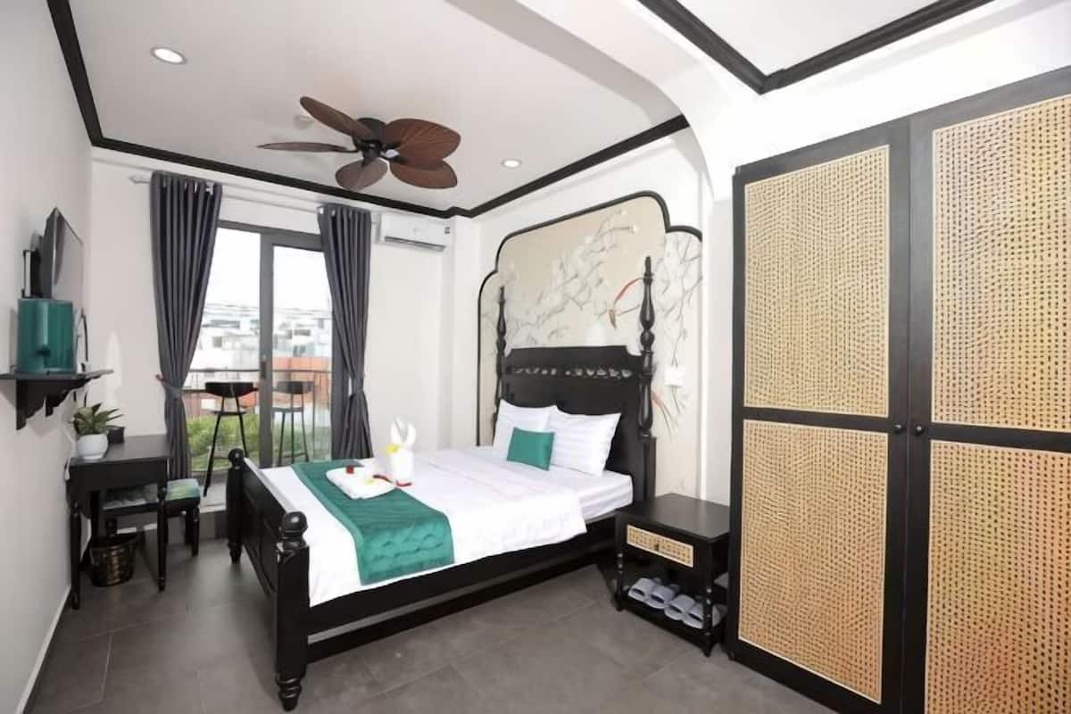 A bedroom with a bed, a ceiling fan, a desk, a chair, a TV, and a view of the city.