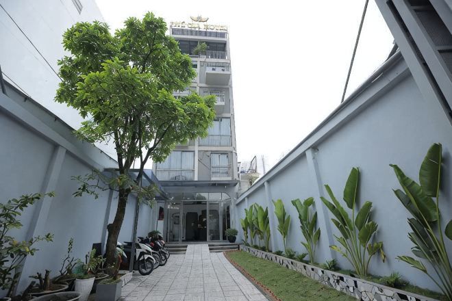 A narrow pathway leading to a building entrance, flanked by potted plants and a tree.