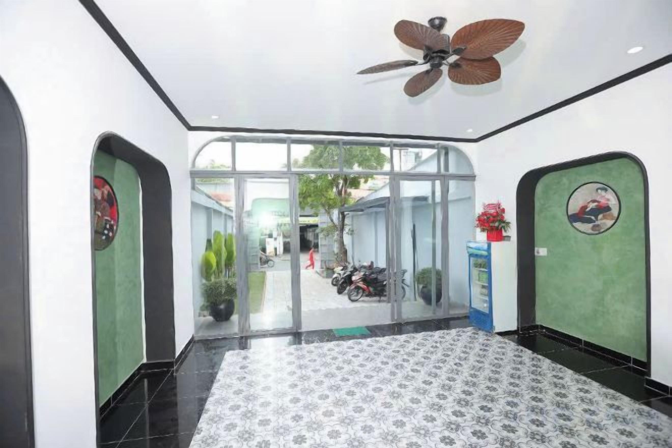 A hotel lobby with a patterned floor, ceiling fan, glass doors leading outside, and a small kiosk with a red flower.