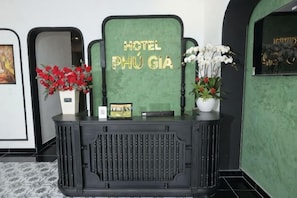 Ein Empfangstresen mit einem Schild, auf dem 'HOTEL PHÚ GIÁ' steht, und zwei Blumenarrangements.