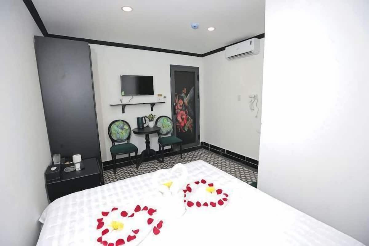 A hotel room with a bed, two chairs, a small table, a TV, and a door with a poster.