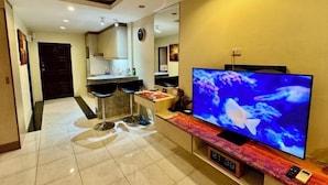 A modern living room with a flat-screen TV, a kitchen area with bar stools, and a dining table. - View talay 6, city center, next to central mall, direct access to the beach (Pattaya)