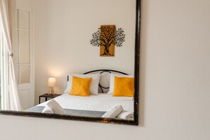 A bedroom with a bed, two pillows, a nightstand with a lamp, and a wall-mounted artwork. - Ionian Luxury Apartments (Corfu)