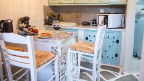 A cozy kitchen with a stone floor, two white chairs with woven seats, a hanging light fixture, and light green cabinets. - Anatoli Studios in Front of the Beach (Corfu)