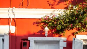 A white door with a small window, a red wall, and a stone-paved entrance. - Anatoli Studios in Front of the Beach (Corfu)