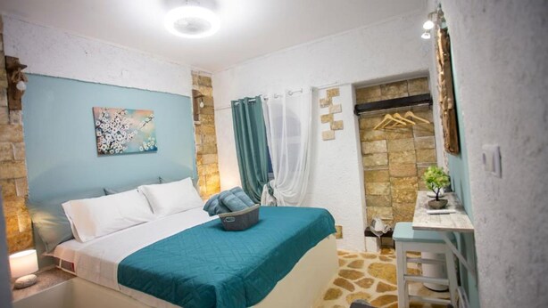 A bedroom with a bed, a nightstand, a small table with a plant, a shower area with a towel rack, and a stone wall. - Anatoli Studios in Front of the Beach (Corfu)