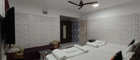 A hotel room with two beds, a TV, a desk, a chair, and a ceiling fan.