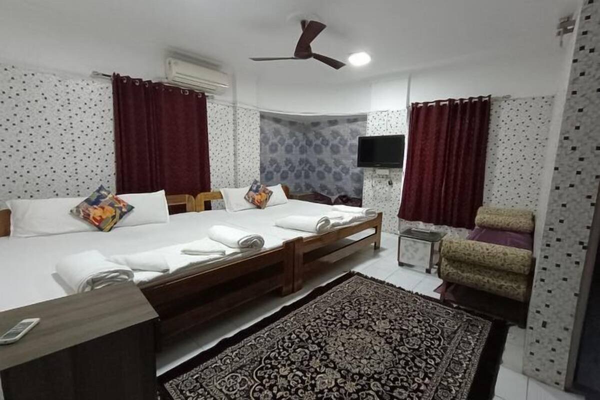 A bedroom with a bed, a TV, a ceiling fan, and a patterned rug.