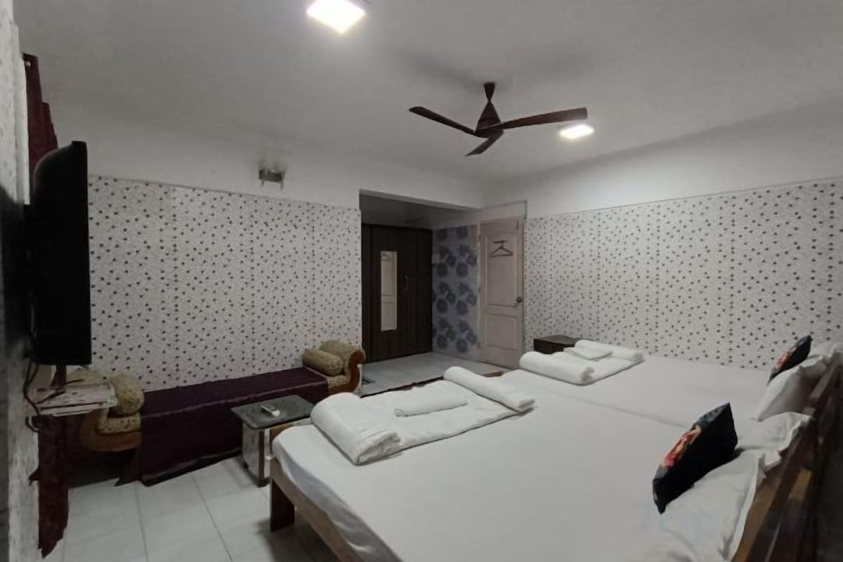 A hotel room with two beds, a desk, a chair, a television, and a ceiling fan.