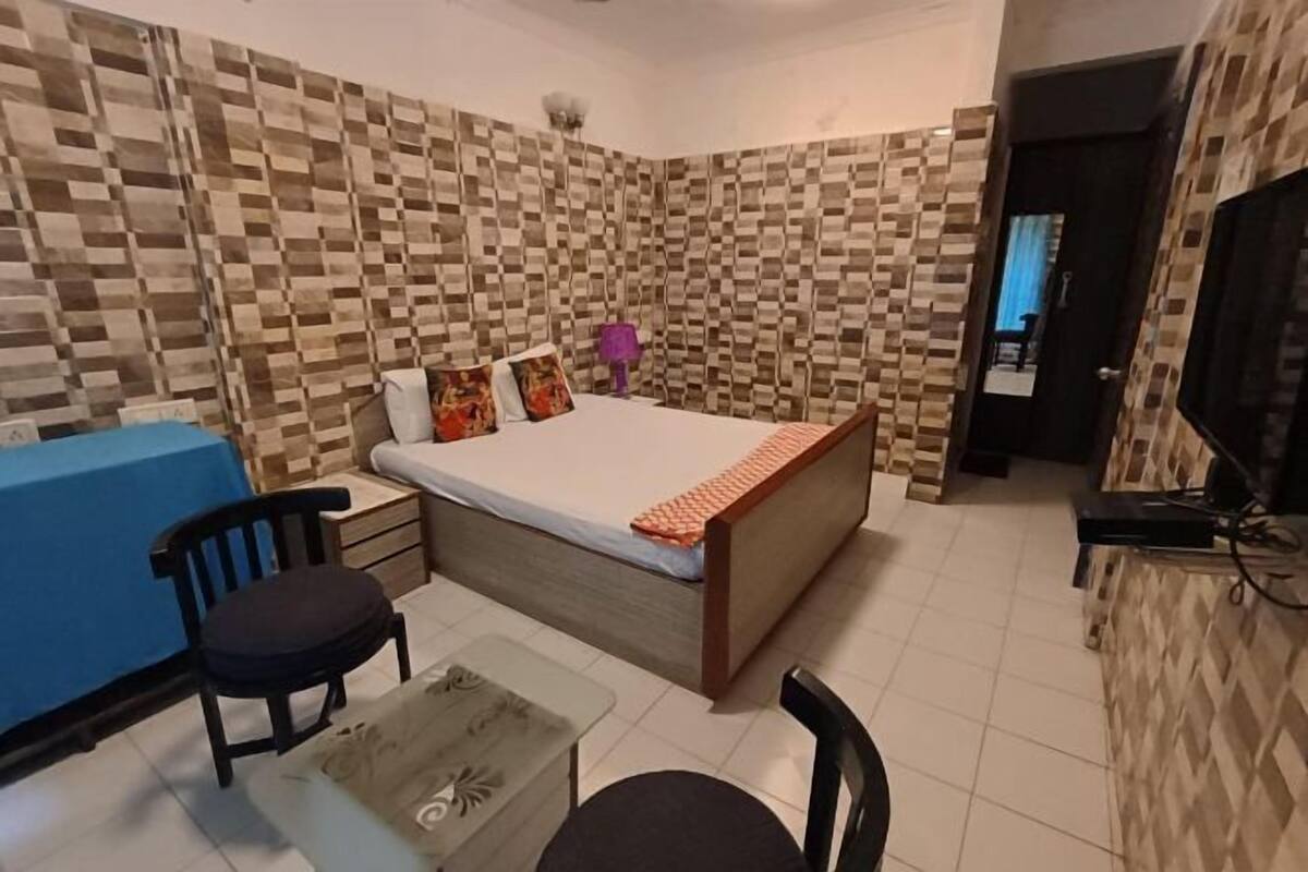 A bedroom with a bed, a desk, two chairs, and a television.