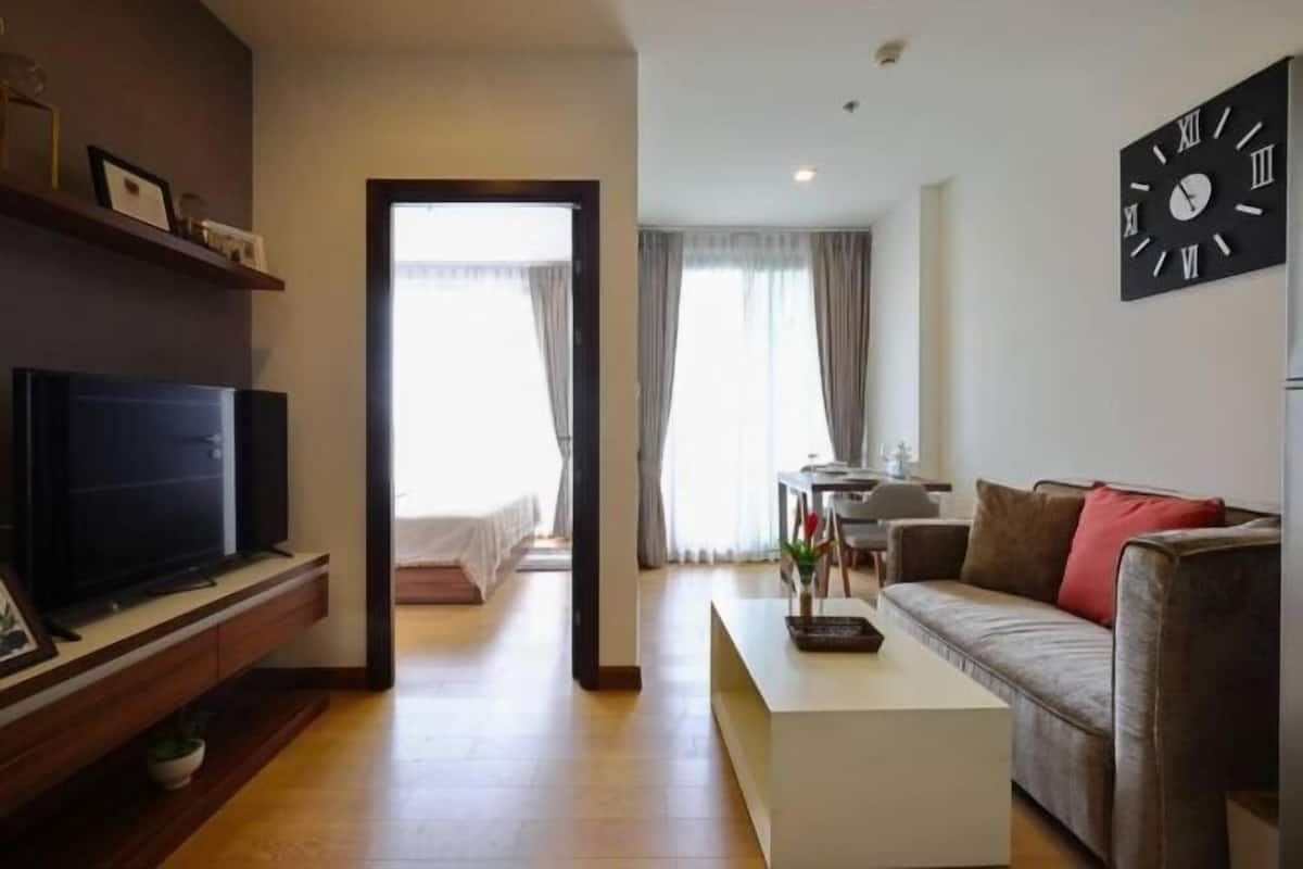 A modern living room with a flat-screen TV, a sofa, a coffee table, and a wall clock.