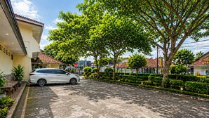 A parking area with a white car, neatly trimmed hedges, and a building with a tiled roof. - Hotel Budi Famili Budget Syariah (Ciamis)