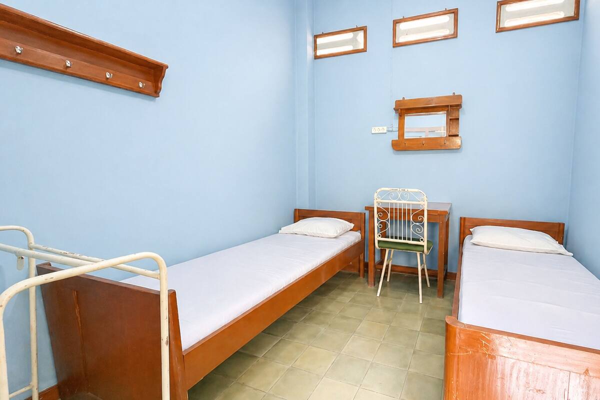 Una habitación con dos camas de madera, una silla, una mesita y un estante en la pared.
