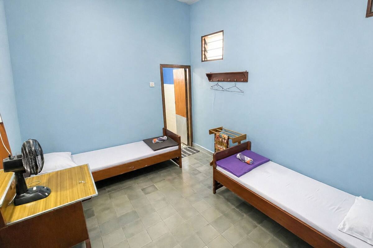 Alojamiento pequeño y con una sola habitación, con dos camas individuales, un escritorio con silla, un ventilador y una pequeña estantería.