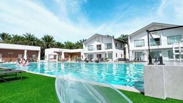 A swimming pool area with a water slide, lounge chairs, and modern buildings in the background.