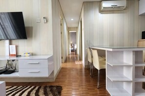A hotel room with a flat-screen TV, a desk with chairs, a white wardrobe, and a built-in shelf unit. - Trivium Terrace Apartment Lippo Cikarang (Min Stay 3 Nights) (South Cikarang)
