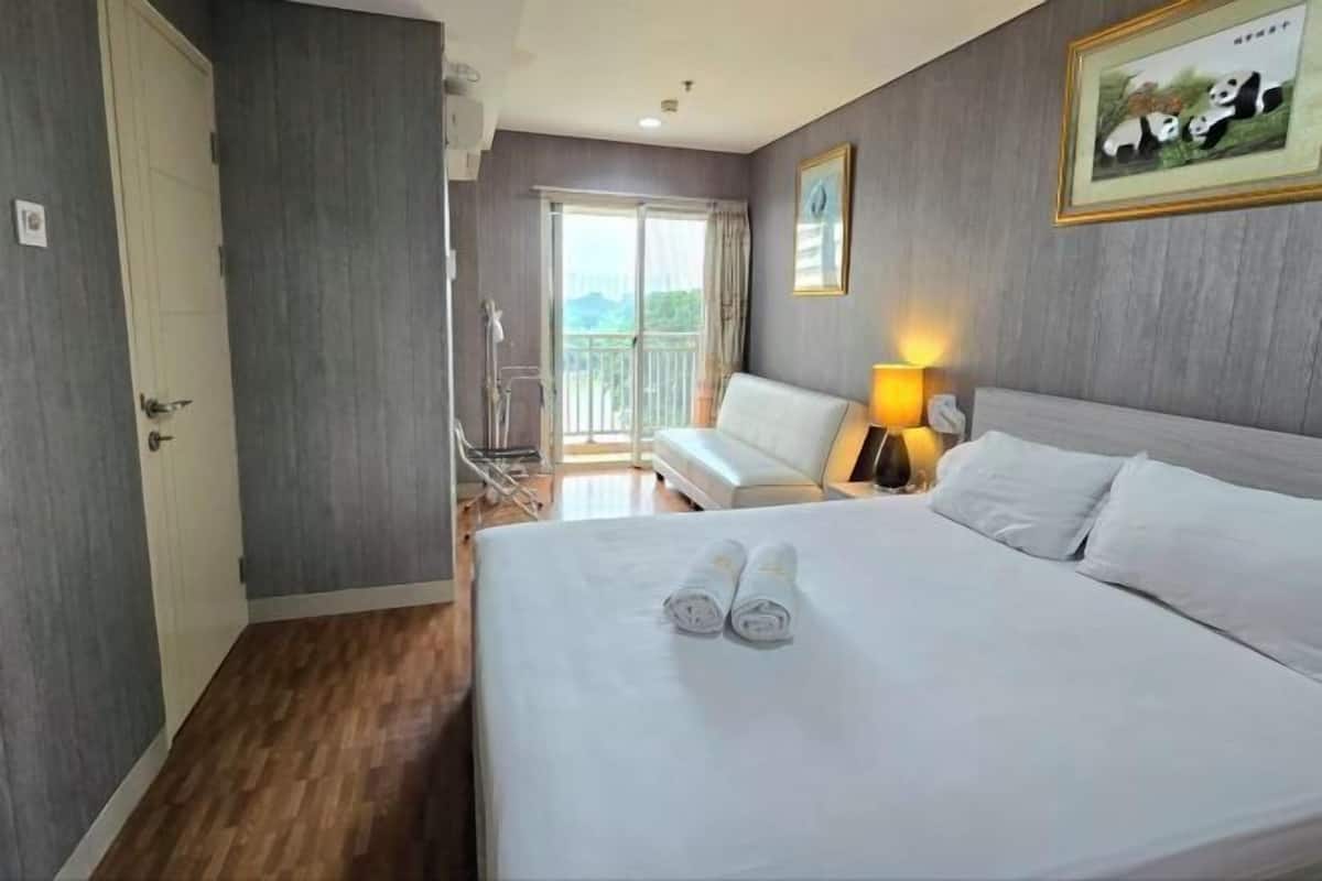 A hotel room with a bed, a sofa, a lamp, and a door.