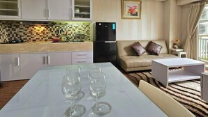 A modern kitchen with white cabinets, a black refrigerator, and a dining area with a table and three wine glasses. - Trivium Terrace Apartment Lippo Cikarang (Min Stay 3 Nights) (South Cikarang)