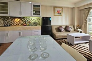 A modern kitchen with white cabinets, a black refrigerator, and a dining area with a table and three wine glasses. - Trivium Terrace Apartment Lippo Cikarang (Min Stay 3 Nights) (South Cikarang)