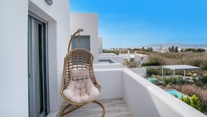 Un balcón con una silla de mimbre, una piscina y vistas al paisaje.