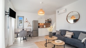 Una sala de estar moderna con un sofá, dos mesas auxiliares, un televisor y una zona de cocina.