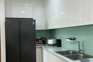 A modern kitchen with white cabinets, a stainless steel refrigerator, a sink, and a countertop with a toaster and a coffee maker.