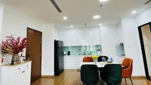 A modern kitchen with white cabinets, a black refrigerator, and a dining area with two chairs and a table. - Vinhomes Royal City Apartments - Sunhometel (Hanoi)