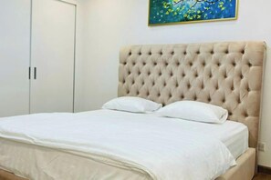 Un lit avec une tête de lit capitonnée, un couvre-lit blanc et deux oreillers.