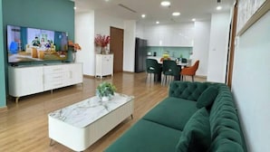 A modern living room with a green sofa, a white coffee table, and a TV on the wall. - Vinhomes Royal City Apartments - Sunhometel (Hanoi)