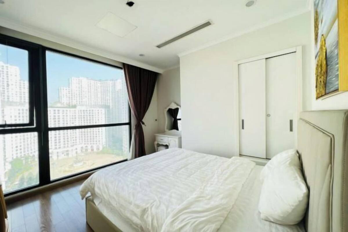A hotel room with a large window, a bed, a nightstand, and a wardrobe.
