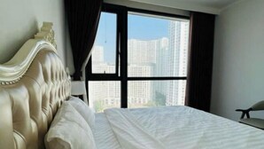 A bedroom with a large bed, a window with curtains, and a view of high-rise buildings. - Vinhomes Royal City Apartments - Sunhometel (Hanoi)