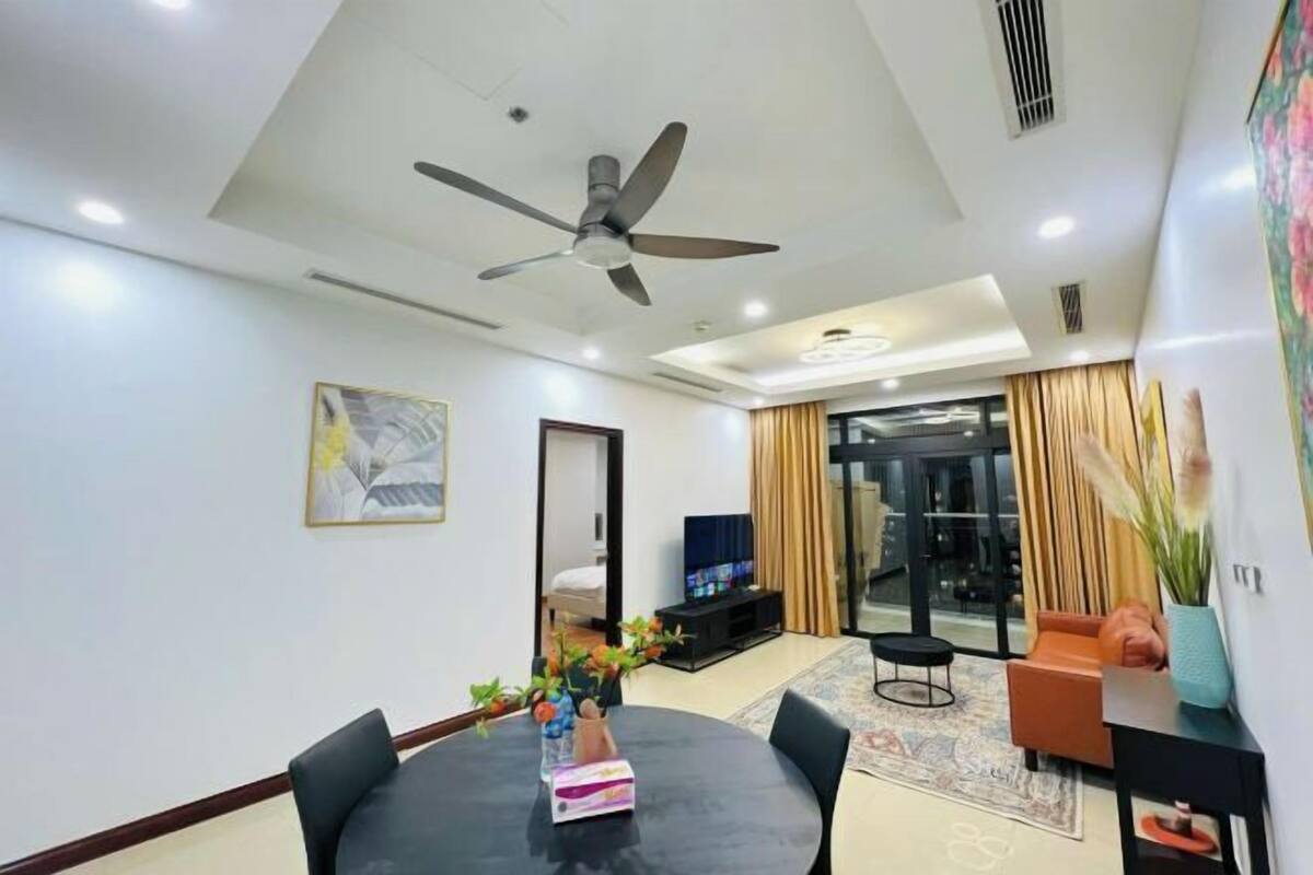 A modern living room with a ceiling fan, a dining table with chairs, a television, and a large window with curtains.