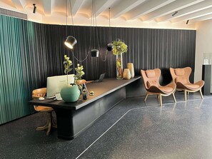A modern reception area with a curved desk, two chairs, a plant, and a decorative vase. - Hotel Al Caminetto Worldhotels Crafted (Torri del Benaco)