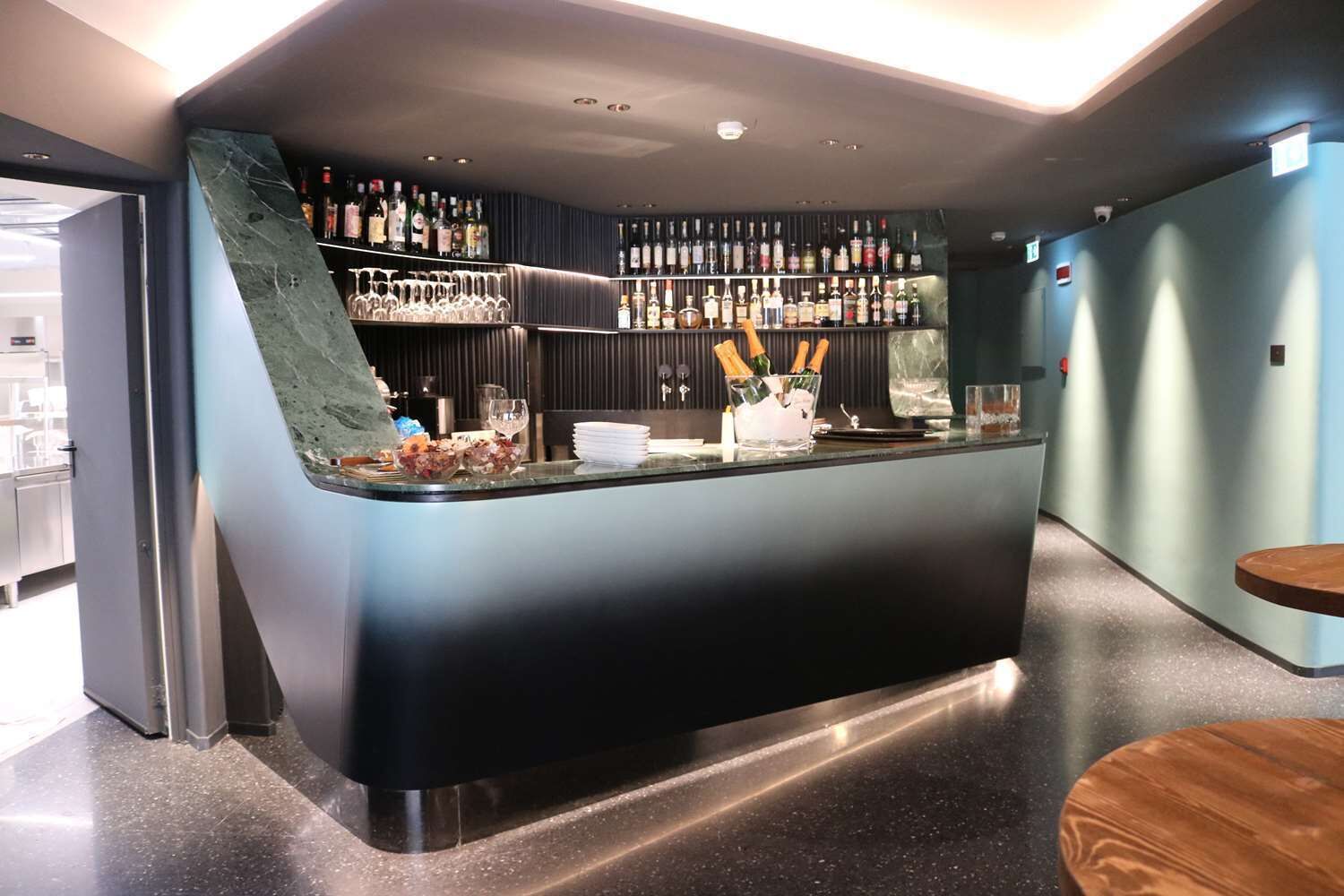 Zona de bar con una barra curva, estantes llenos de botellas y un pequeño espacio para sentarse.