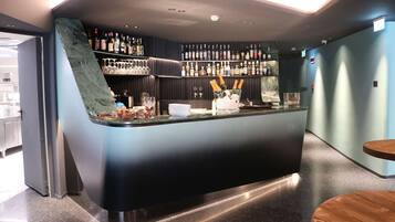 Zona de bar con una barra curva, estantes llenos de botellas y un pequeño espacio para sentarse.