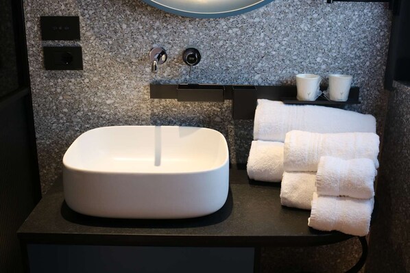A bathroom with a white sink, two faucets, a towel rack with folded towels, and a wall-mounted light fixture. - Hotel Al Caminetto Worldhotels Crafted (Torri del Benaco)