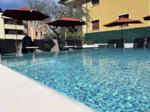 Una piscina con agua cristalina, rodeada de sillas de descanso y sombrillas rojas.