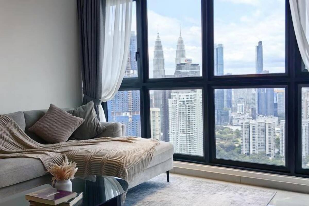 A modern living room with a large window, a grey sofa, and a view of high-rise buildings.