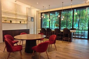 A modern dining area with a round table and red chairs, large windows with a view of greenery, and pendant lighting. - TRX AGILE Bukit Bintang Superior 8 Pax Family Suites (Kuala Lumpur)