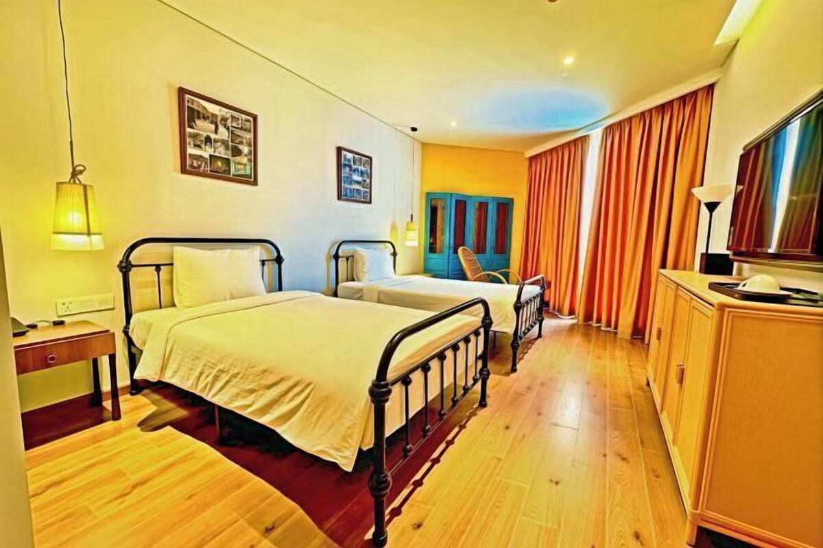 A hotel room with two beds, a wooden floor, a desk, a chair, a TV, and a window with curtains.