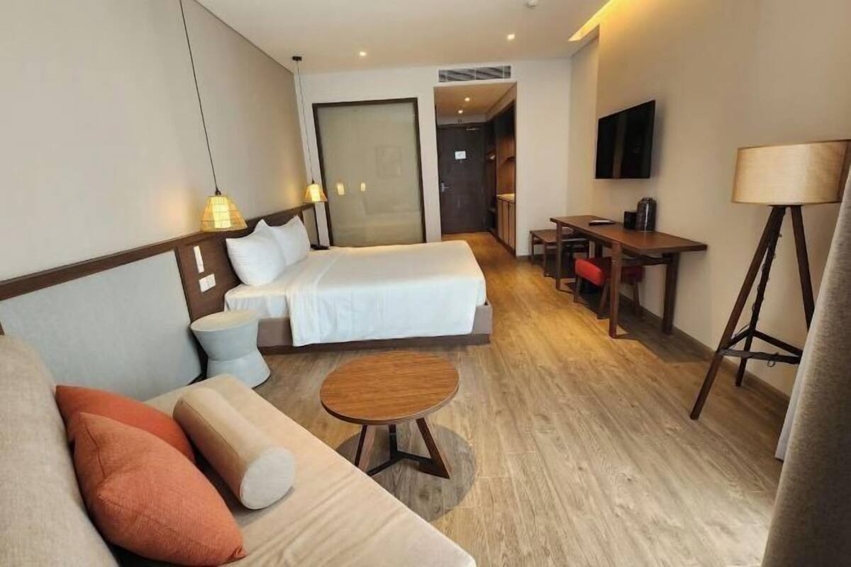 A hotel room with a bed, a sofa, a small table, a TV, and a lamp.
